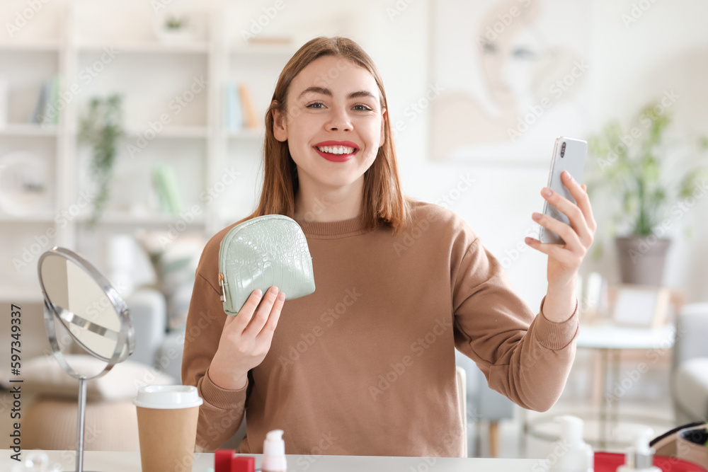 Young woman with cosmetic bag and mobile phone at home