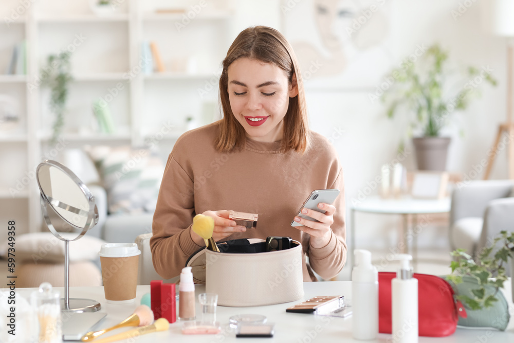 Young woman with makeup product and mobile phone at home