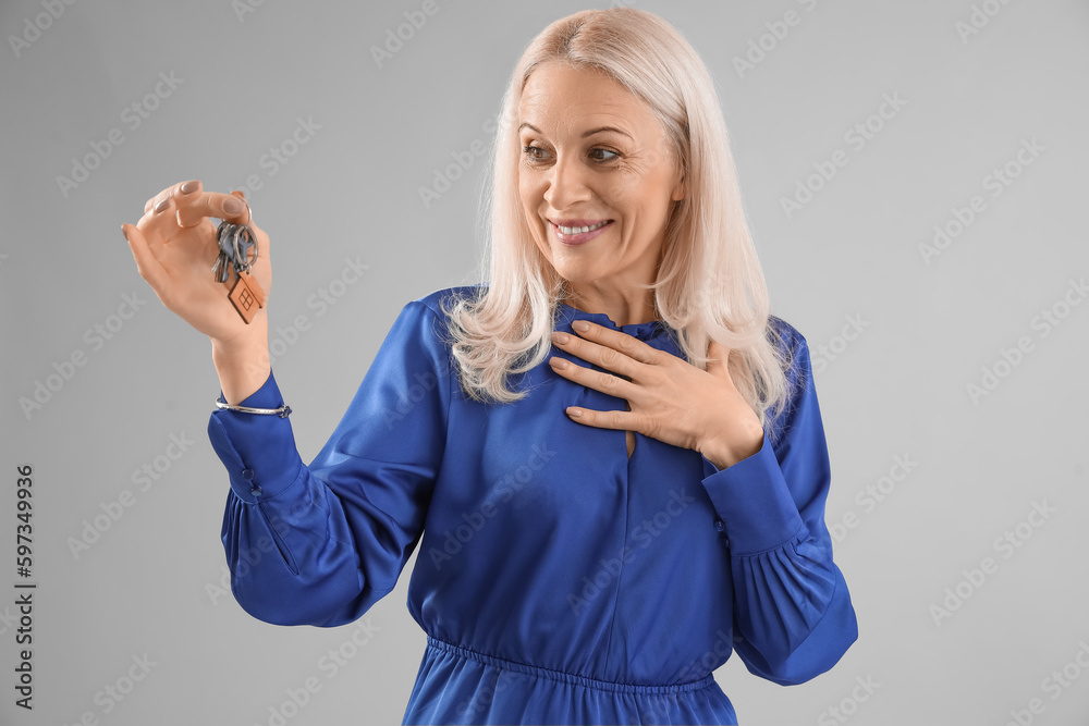 Mature woman with keys from house on grey background