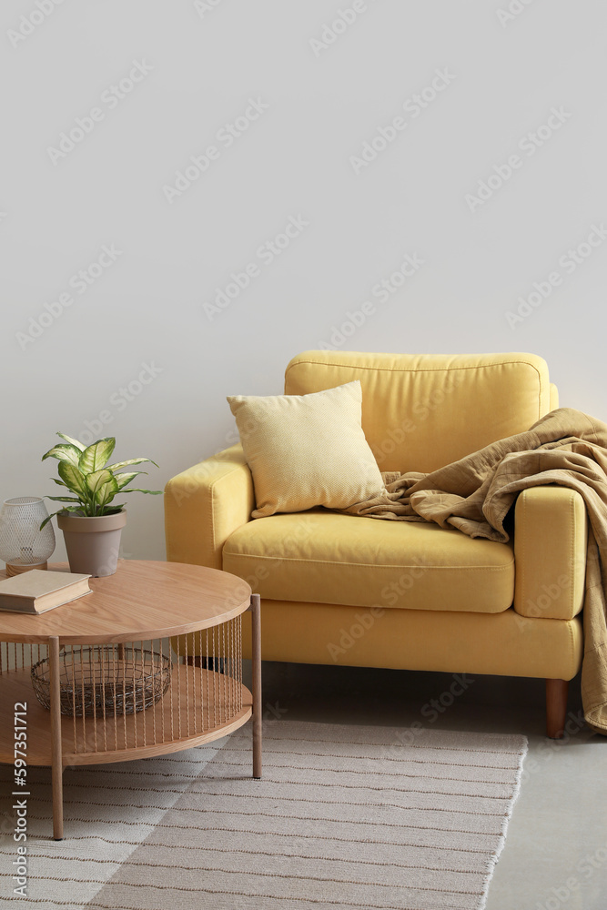 Cozy yellow armchair with cushion and coffee table near white wall