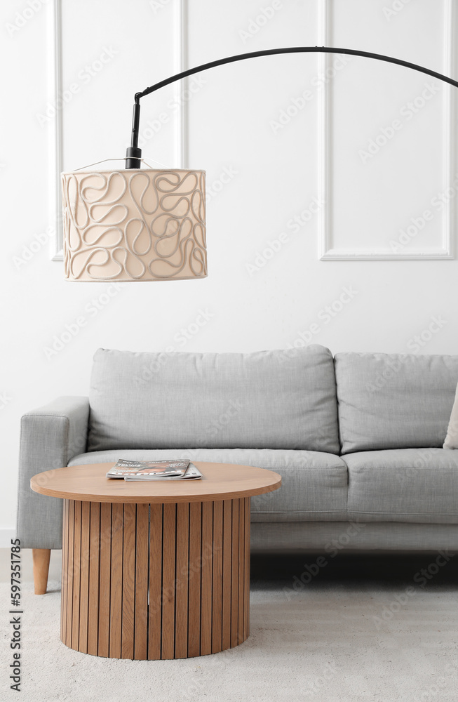 Cozy grey sofa, coffee table and lamp near white wall