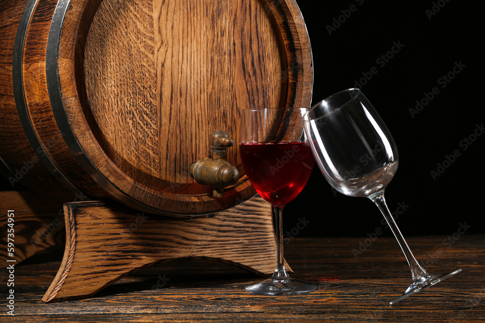 Wooden barrel with glasses of wine on table against dark background