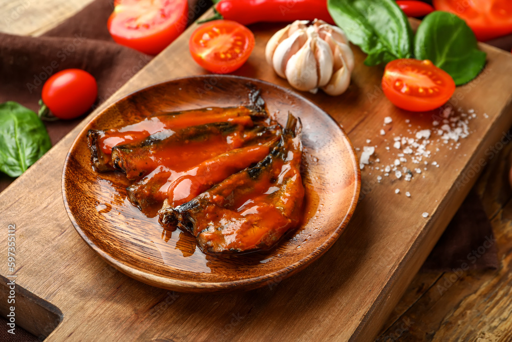 Board with canned fish in tomato sauce and vegetables on wooden table