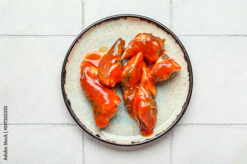 Plate with canned fish in tomato sauce on white tiled table