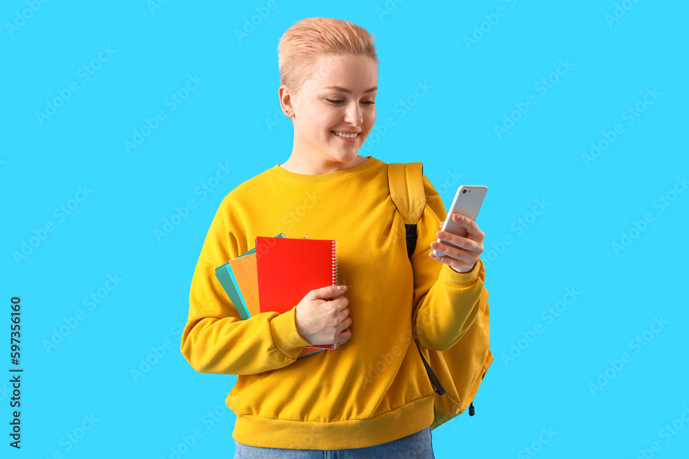 Female student with notebooks using mobile phone on blue background