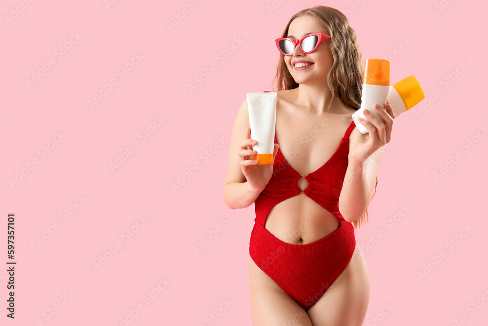 Beautiful young woman with sunscreen creams on pink background