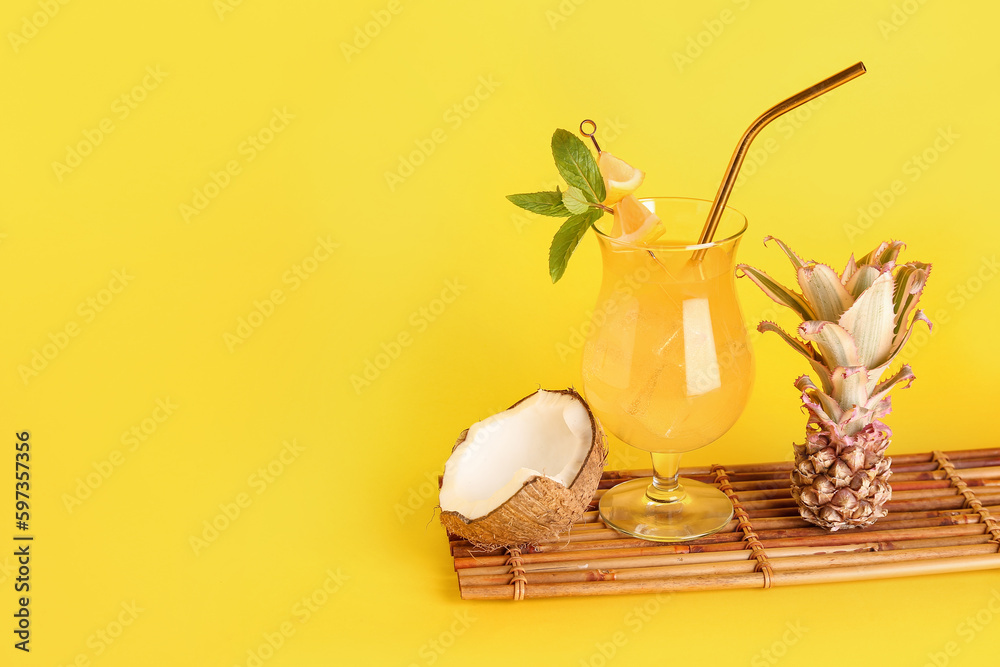 Glass of cocktail with baby pineapple and coconut on yellow background