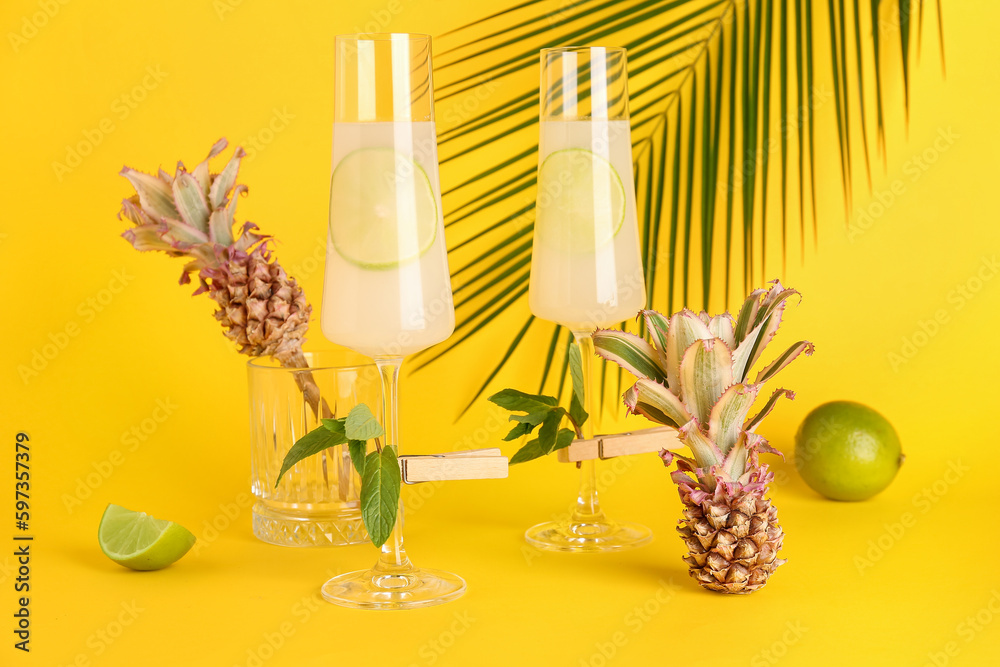 Glasses of cocktail with lime, mint and baby pineapples on yellow background