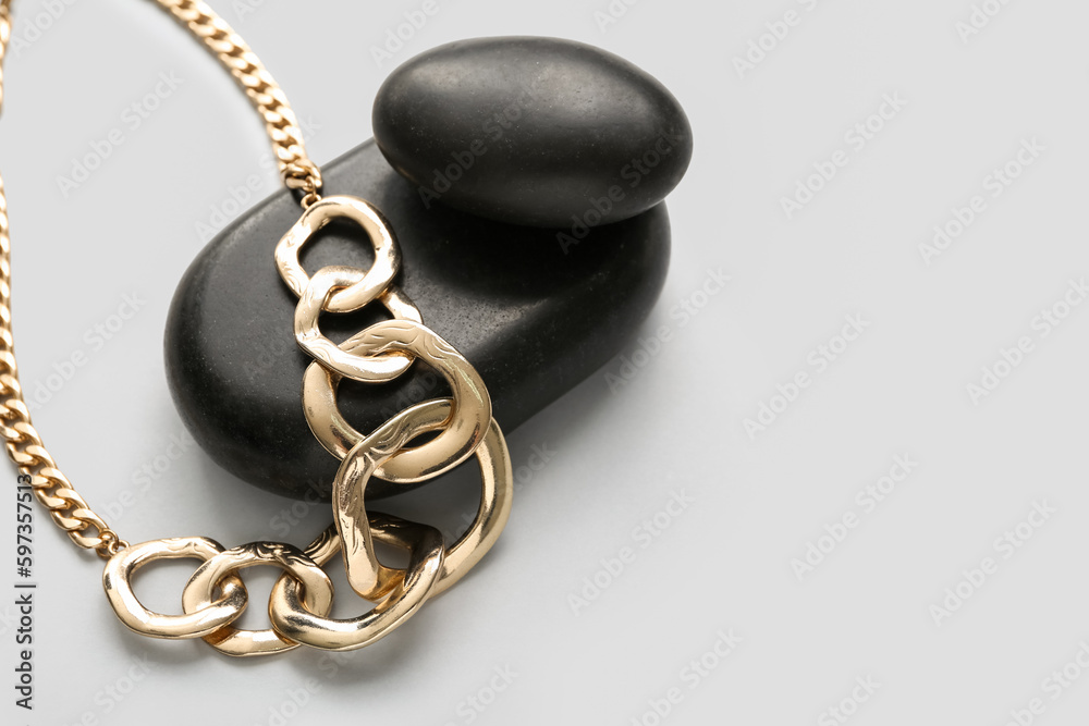 Black stones with golden necklace on light background, closeup