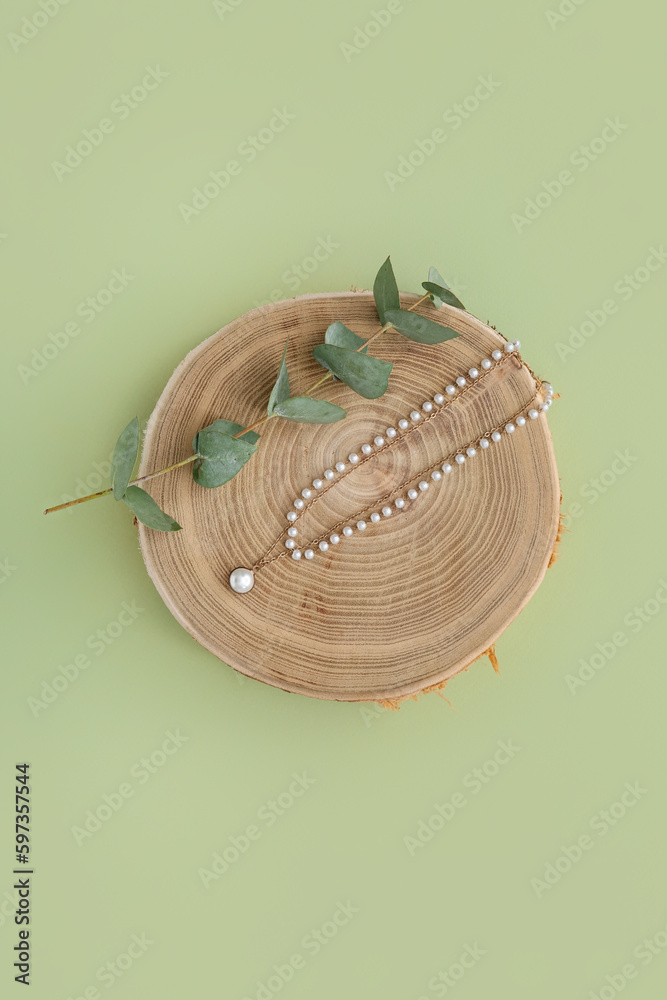 Wooden stand with pearl necklace and eucalyptus branch on green background