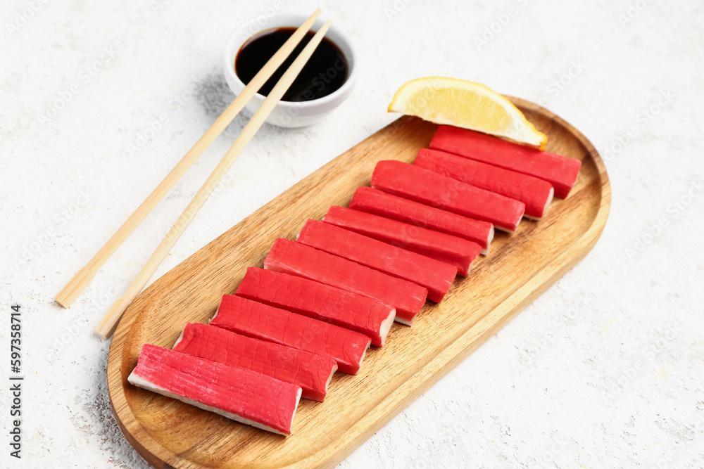 Wooden board with tasty crab sticks on light background