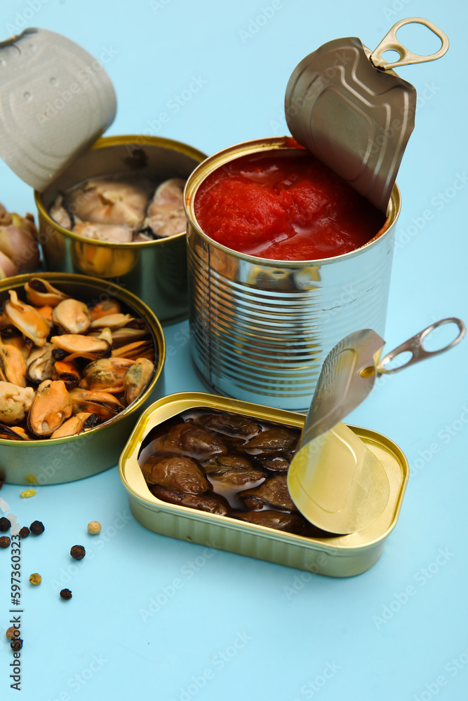 Opened tin cans with mussels and tomato sauce on blue background