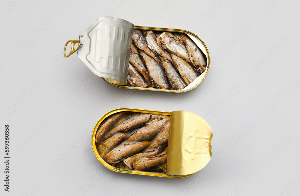 Opened tin cans with sprats in oil on grey background