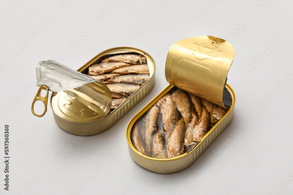 Opened tin cans with sprats in oil on grey background