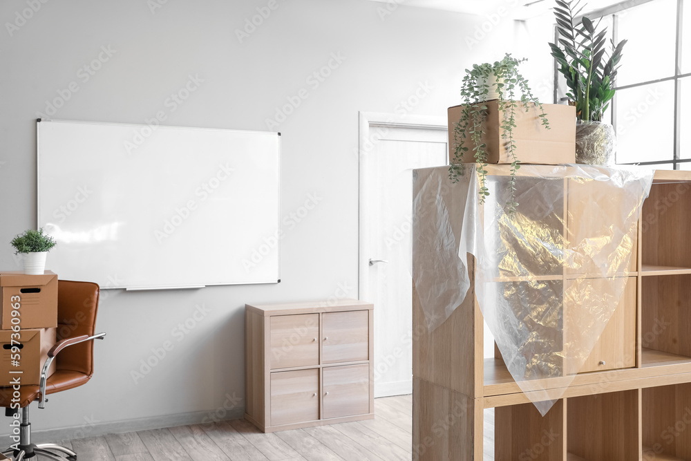 Shelving unit with cardboard box, wrap and plants in office on moving day