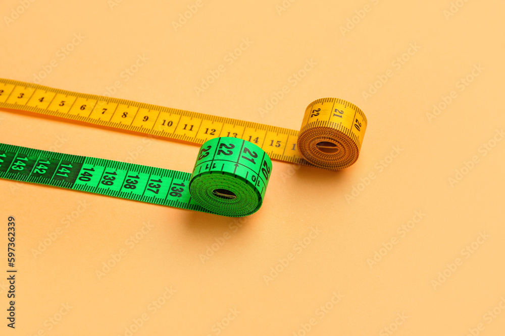 Orange and green measuring tape on color background