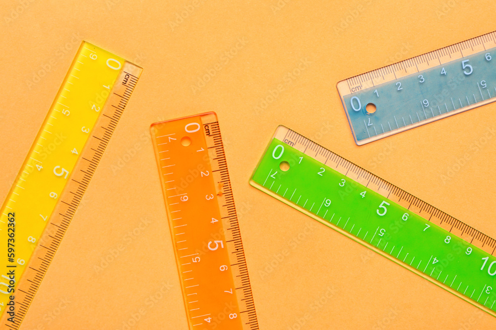 Colorful plastic rulers on orange background