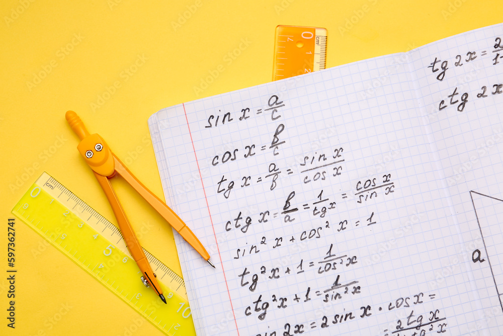 Copybook with maths formulas and stationery on yellow background