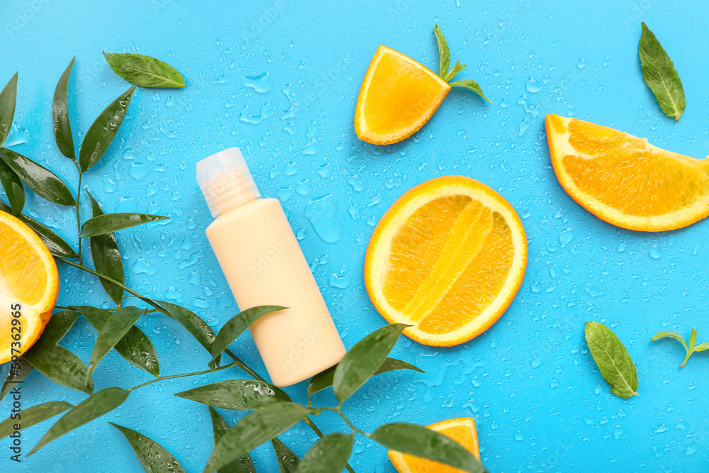 Cosmetic bottle with oranges and plant branch on blue background