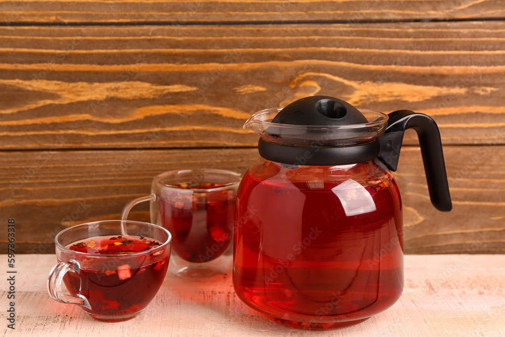 Transparent teapot and cups of fruit tea on white wooden table