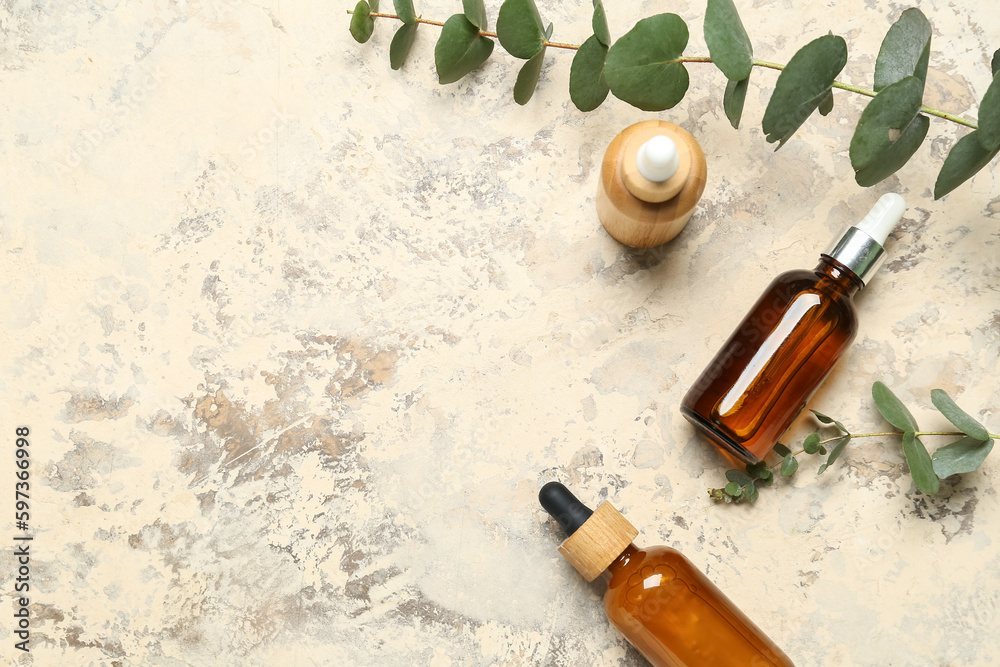 Bottles with cosmetic oil and eucalyptus branches on textured background