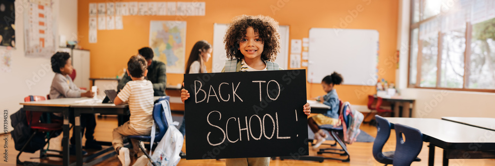 Happy boy holding a back to school sign on his first day back at school