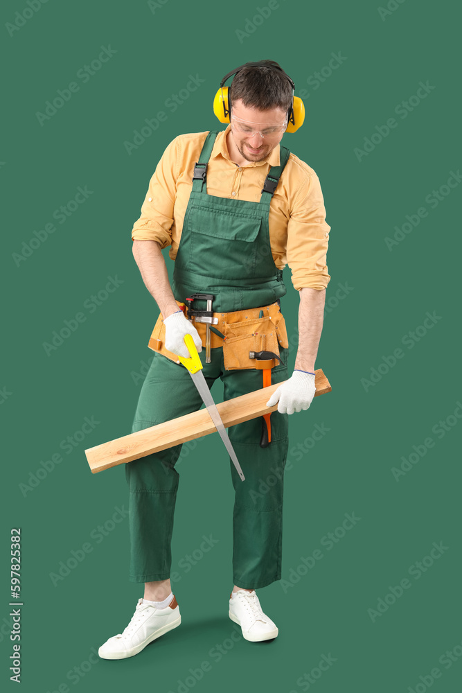 Male carpenter sawing wooden plank on green background