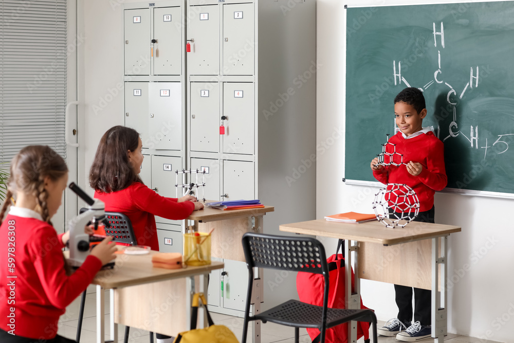 Little boy with molecular model having Chemistry lesson near blackboard in science classroom