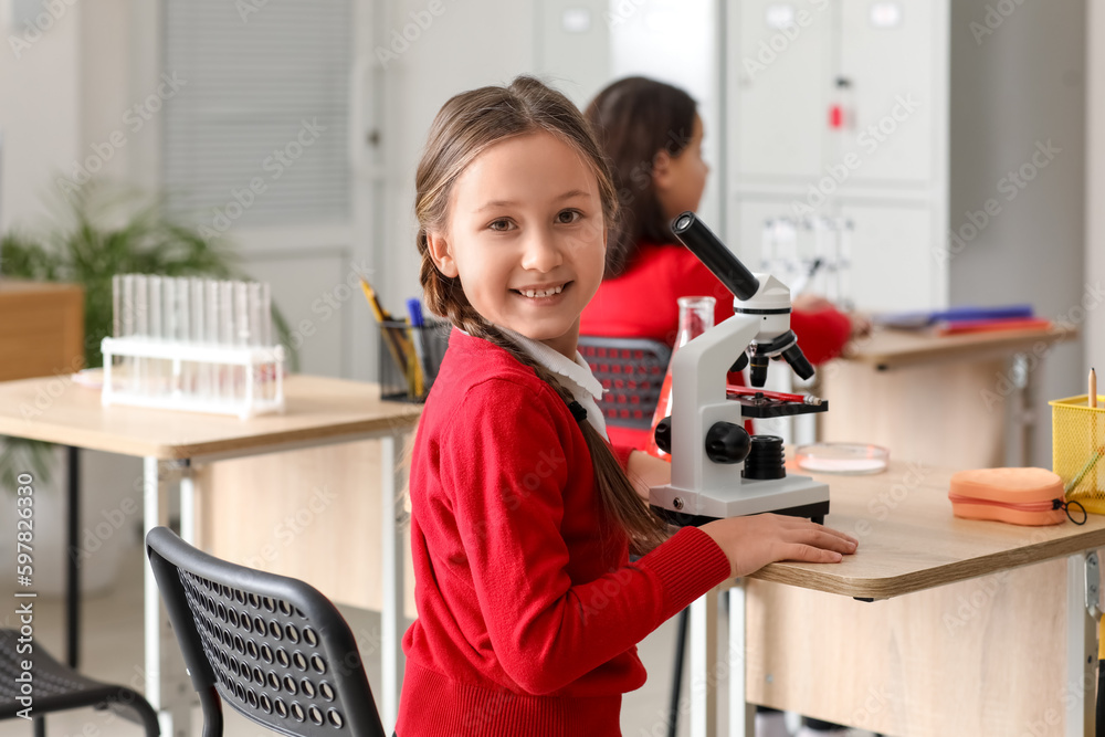 Little girl with microscope having Chemistry lesson in science classroom