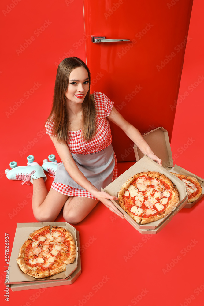 Young woman in roller skates with tasty pizza and fridge on red background