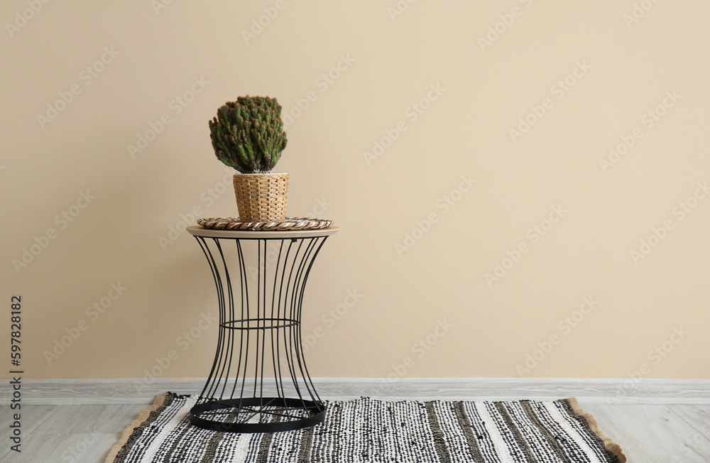 Cactus in wicker pot on table near beige wall