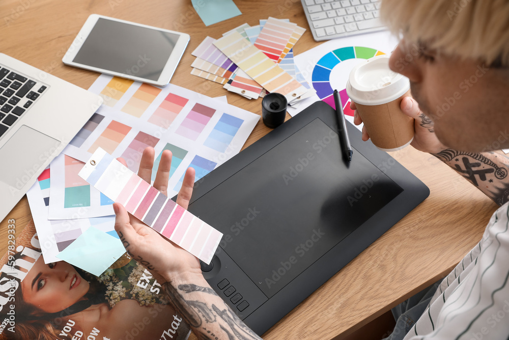 Tattooed graphic designer with paint palette and cup of coffee at table in office, closeup