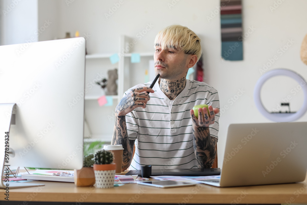 Tattooed graphic designer with apple working at table in office