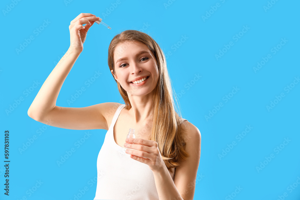 Young woman using serum for hair growth on blue background