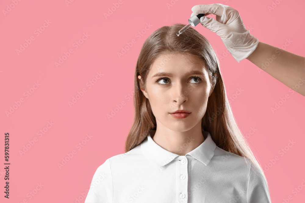 Cosmetologist applying serum on young womans hair against pink background