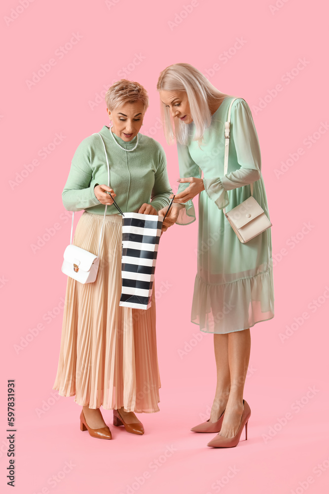 Mature women with shopping bag on pink background