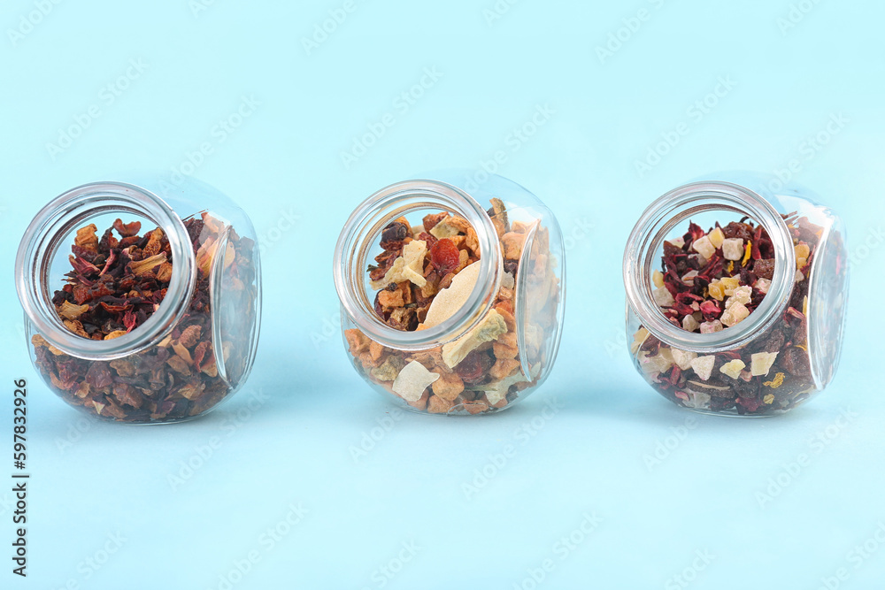 Jars with different dried fruit tea on blue background