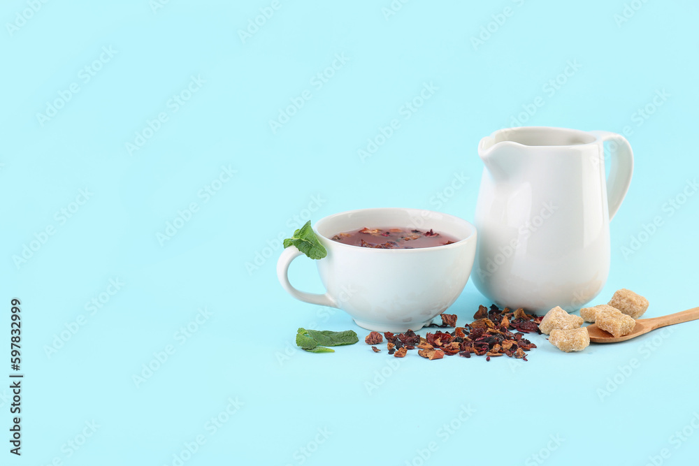 Glass of fruit tea, pitcher and snacks on blue background