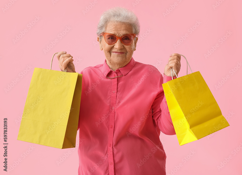 Senior woman with shopping bags on pink background