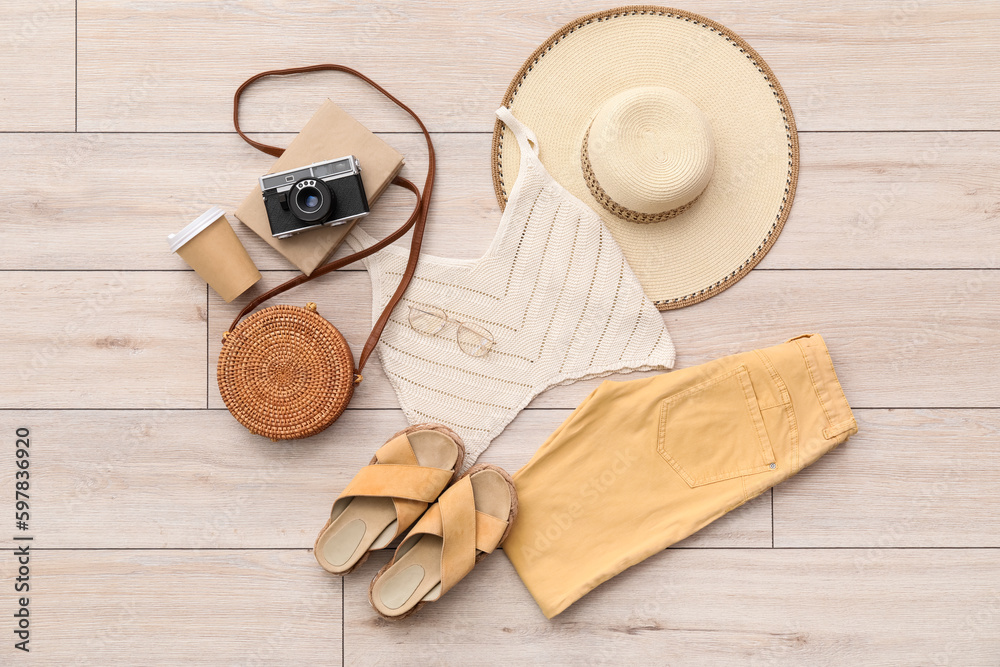 Summer clothes with accessories, cup of coffee and photo camera on light wooden floor