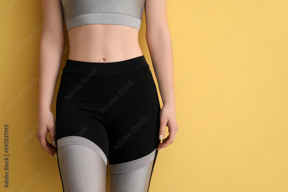 Sporty young woman in leggings on yellow background, closeup