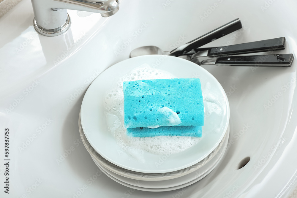 Plates with cleaning sponge and cutlery in sink, closeup