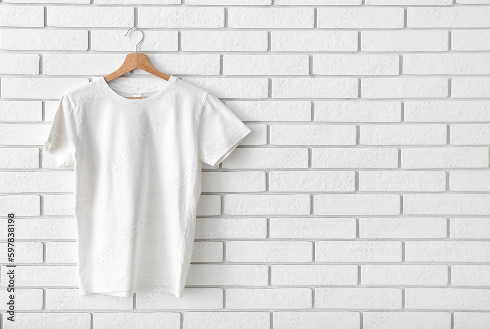 Stylish t-shirt hanging on white brick wall