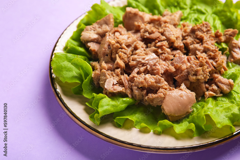 Plate with delicious canned tuna and fresh lettuce on lilac background