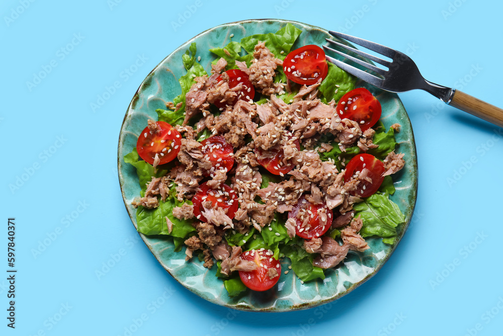 Plate with delicious tuna salad and fork on blue background