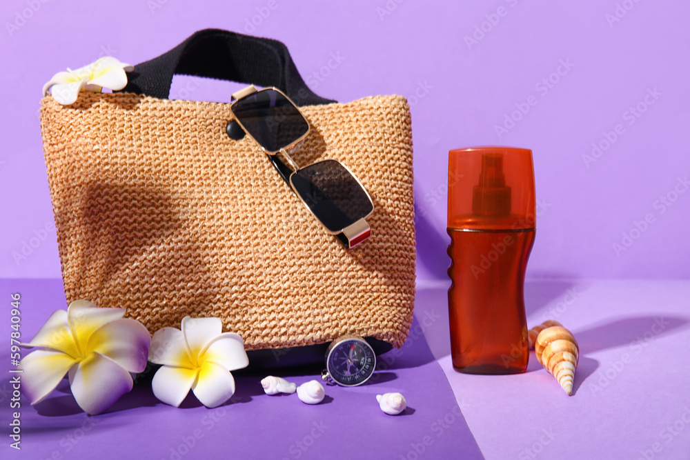 Wicker bag, sunglasses, bottle of sunscreen, compass and plumeria flowers on lilac background