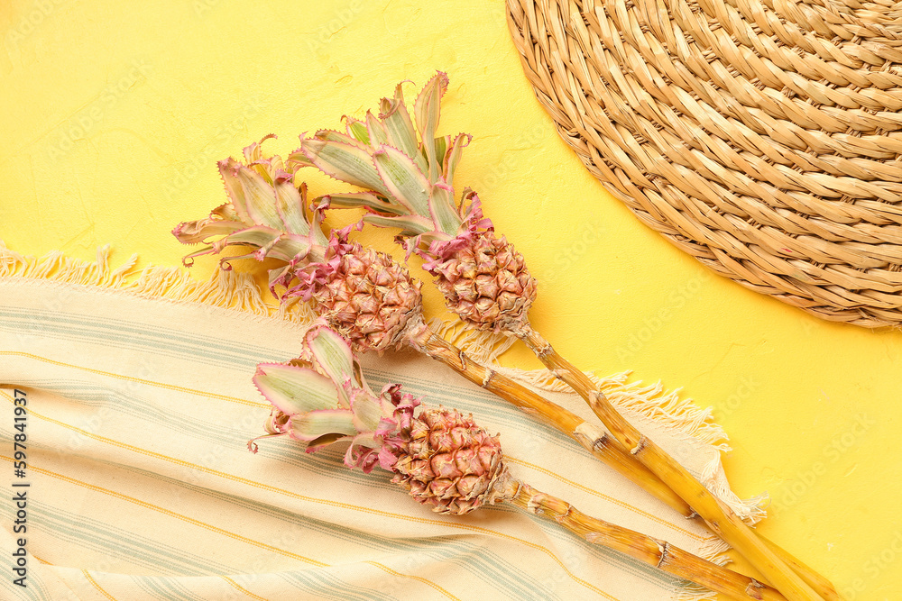 Decorative pineapples with cloth and wicker mat on yellow background