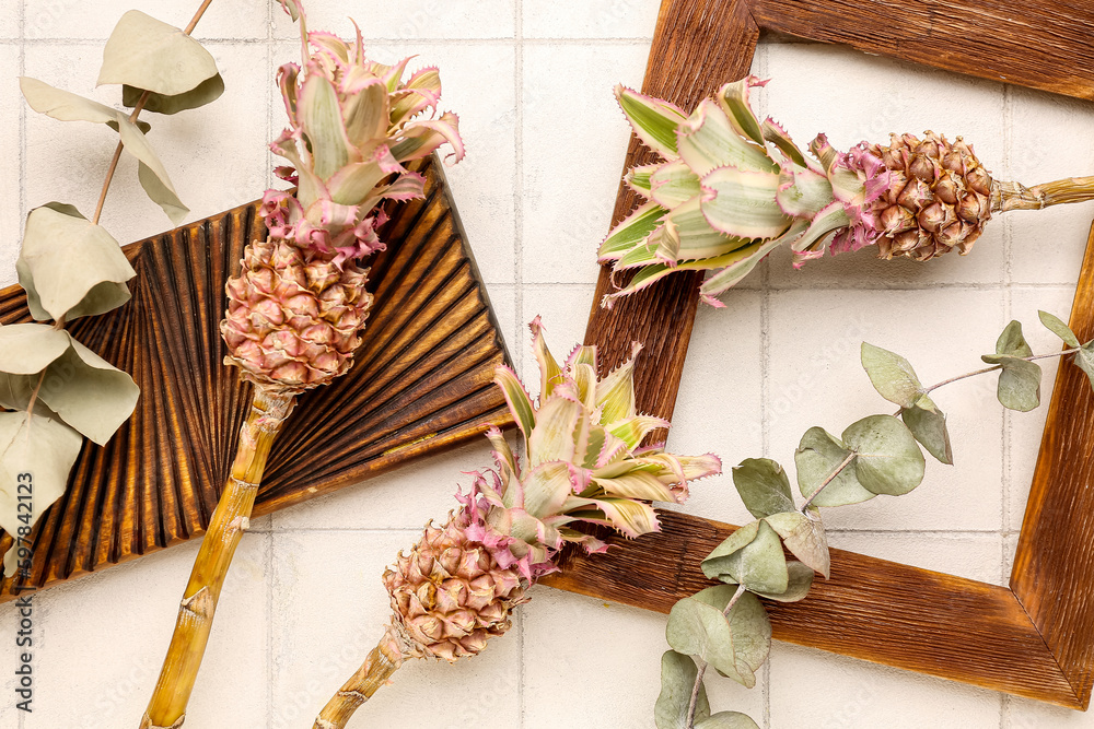 Decorative pineapples with eucalyptus branches, frame and board on white tile background