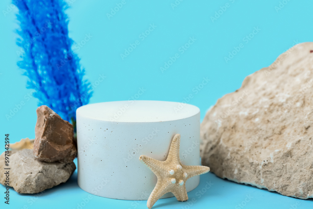 Decorative plaster podium, starfish, stones and seaweed on blue background