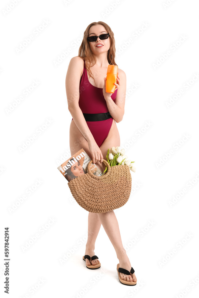 Beautiful young woman with sunscreen cream and beach bag on white background